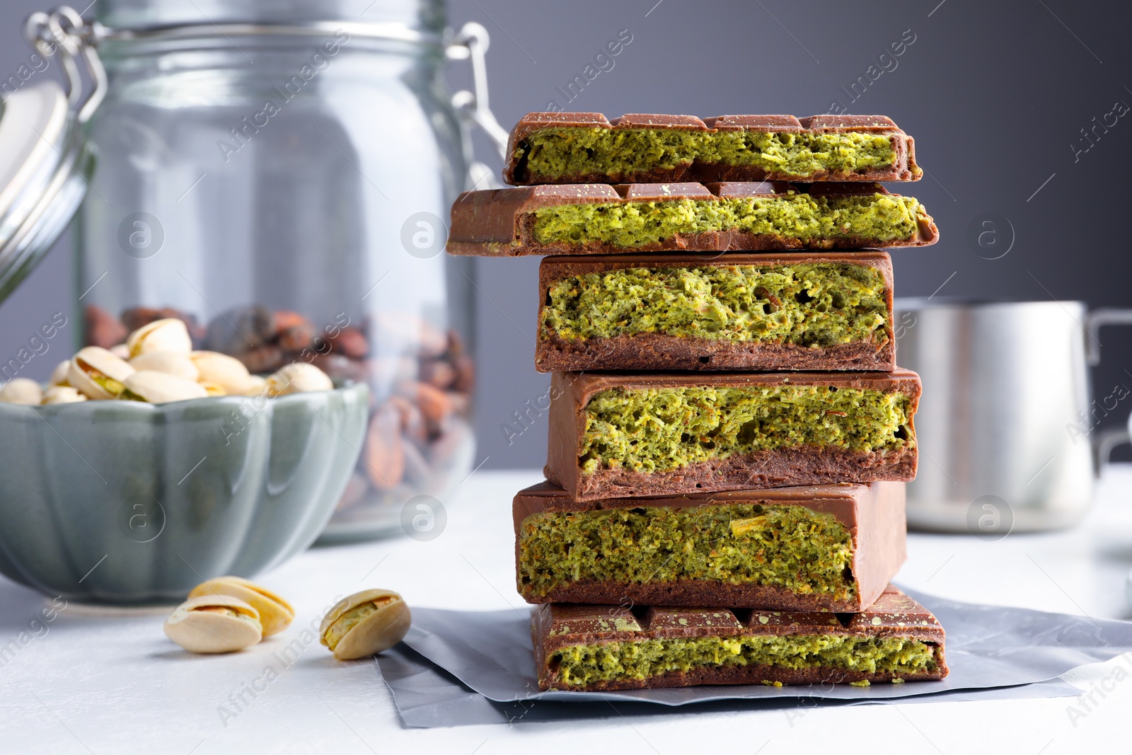 Pieces of delicious Dubai chocolate with pistachios, knafeh and cocoa beans on white table, closeup Photo of Pieces of delicious Dubai chocolate with pistachios, knafeh and cocoa beans on white table, closeup