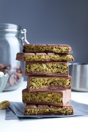 Photo of Pieces of delicious Dubai chocolate with pistachios, knafeh and cocoa beans on white table, closeup