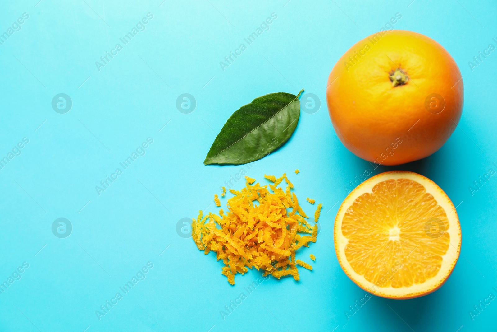 Photo of Pile of fresh orange zest, fruits and leaf on light blue background, flat lay. Space for text