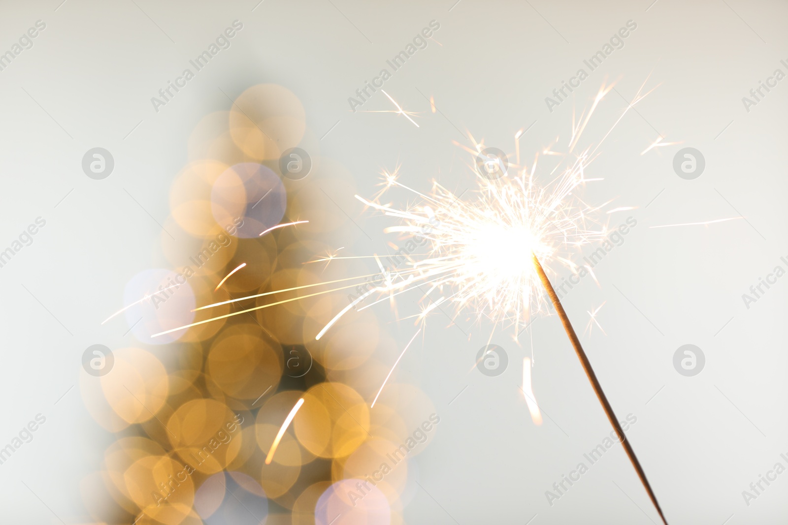 Photo of Bright burning sparkler on light background with blurred lights, closeup. Bokeh effect