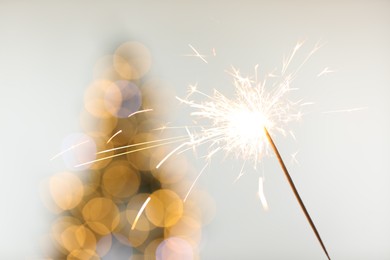 Photo of Bright burning sparkler on light background with blurred lights, closeup. Bokeh effect