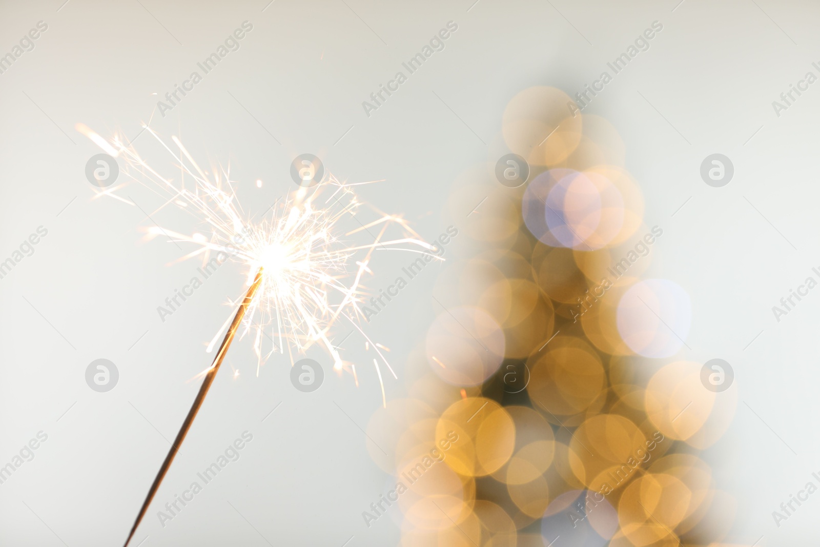 Photo of Bright burning sparkler on light background with blurred lights, closeup. Bokeh effect