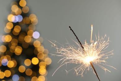 Photo of Bright burning sparkler on grey background with blurred lights, closeup. Bokeh effect