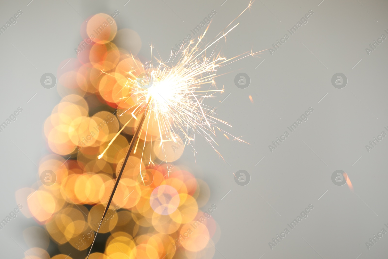 Photo of Bright burning sparkler on grey background with blurred lights, closeup. Bokeh effect