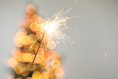 Photo of Bright burning sparkler on grey background with blurred lights, closeup. Bokeh effect