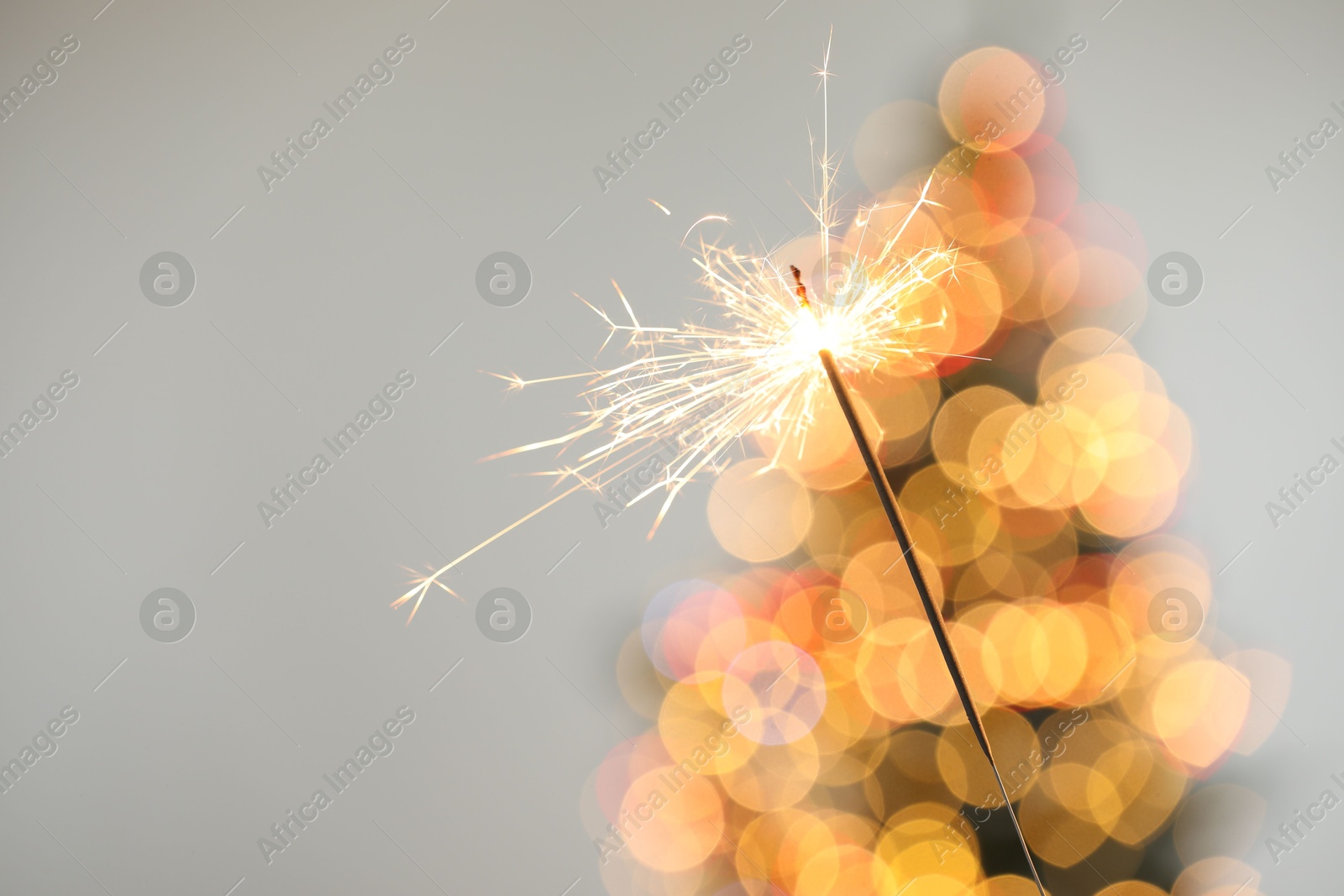 Photo of Bright burning sparkler on grey background with blurred lights, closeup. Bokeh effect