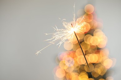 Photo of Bright burning sparkler on grey background with blurred lights, closeup. Bokeh effect