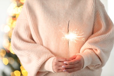 Photo of Woman with bright burning sparkler on blurred background, closeup. Bokeh effect