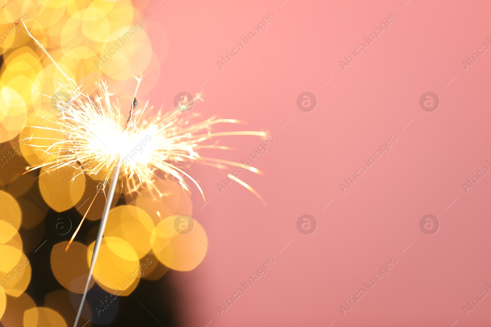 Photo of Bright burning sparkler on pink background with blurred lights, closeup. Bokeh effect