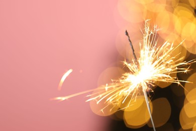 Photo of Bright burning sparkler on pink background with blurred lights, closeup. Bokeh effect