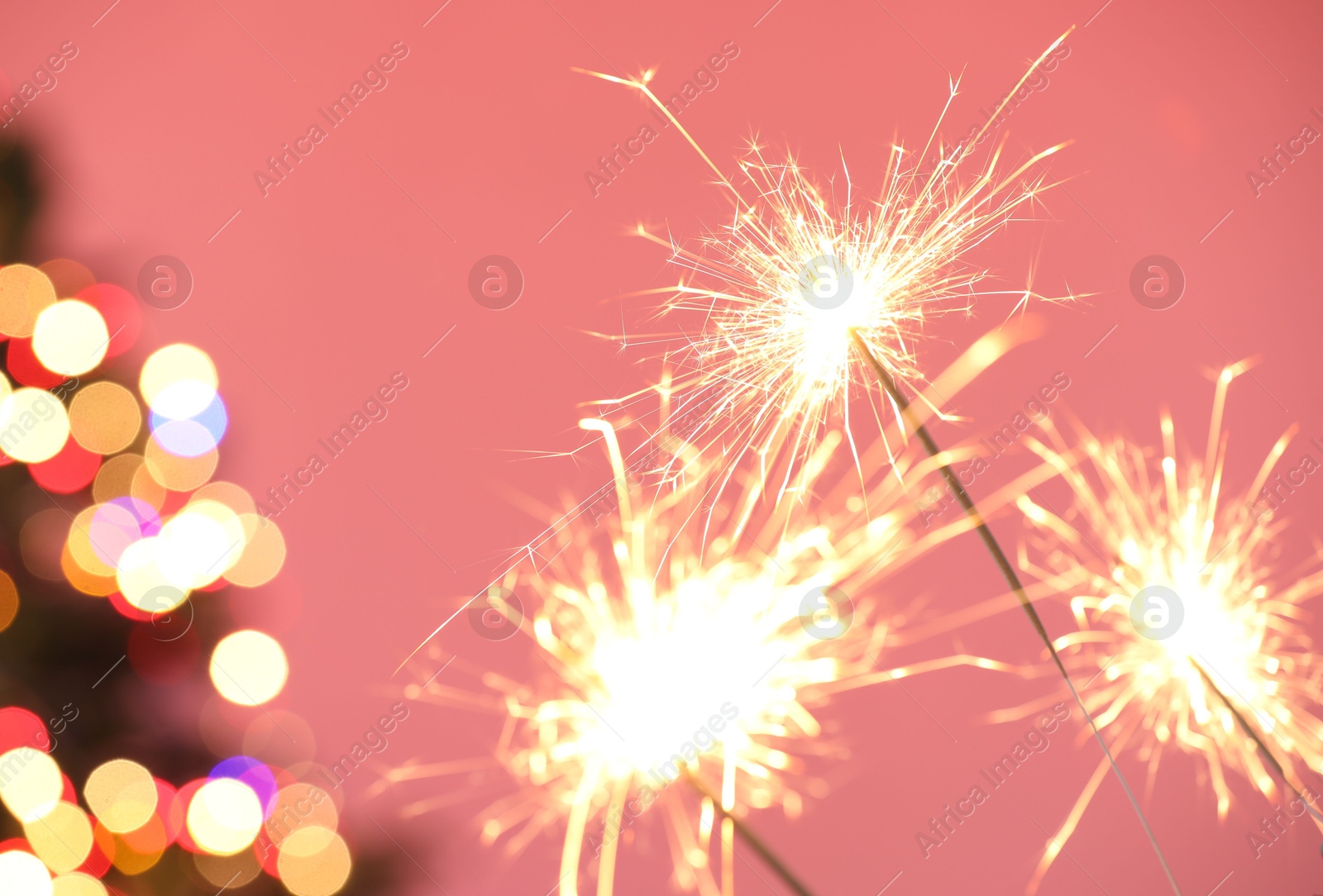 Photo of Bright burning sparklers on pink background with blurred lights, closeup. Bokeh effect