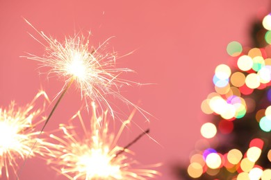 Photo of Bright burning sparklers on pink background with blurred lights, closeup. Bokeh effect