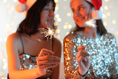 Photo of Women holding bright burning sparklers on background with blurred lights, selective focus