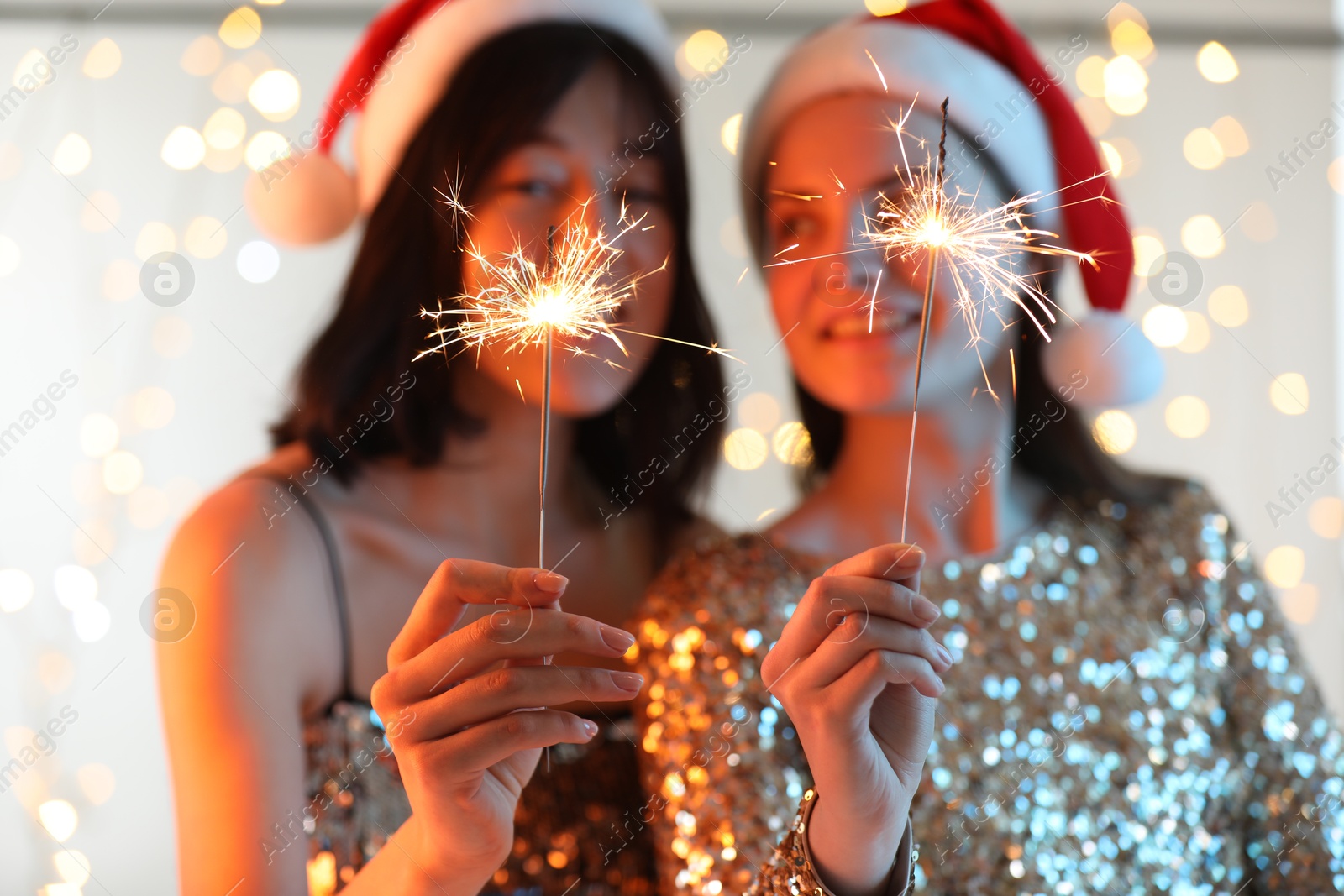 Photo of Women holding bright burning sparklers on background with blurred lights, selective focus