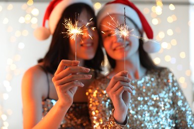 Photo of Women holding bright burning sparklers on background with blurred lights, selective focus