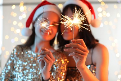 Photo of Women holding bright burning sparklers on background with blurred lights, selective focus