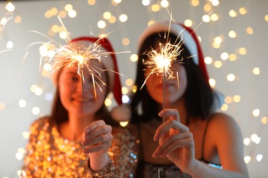 Photo of Women holding bright burning sparklers on background with blurred lights, selective focus