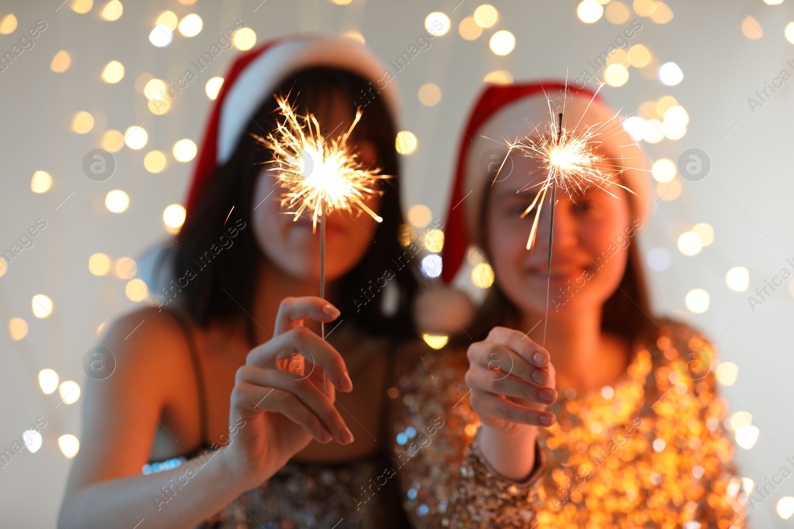 Photo of Women holding bright burning sparklers on background with blurred lights, selective focus