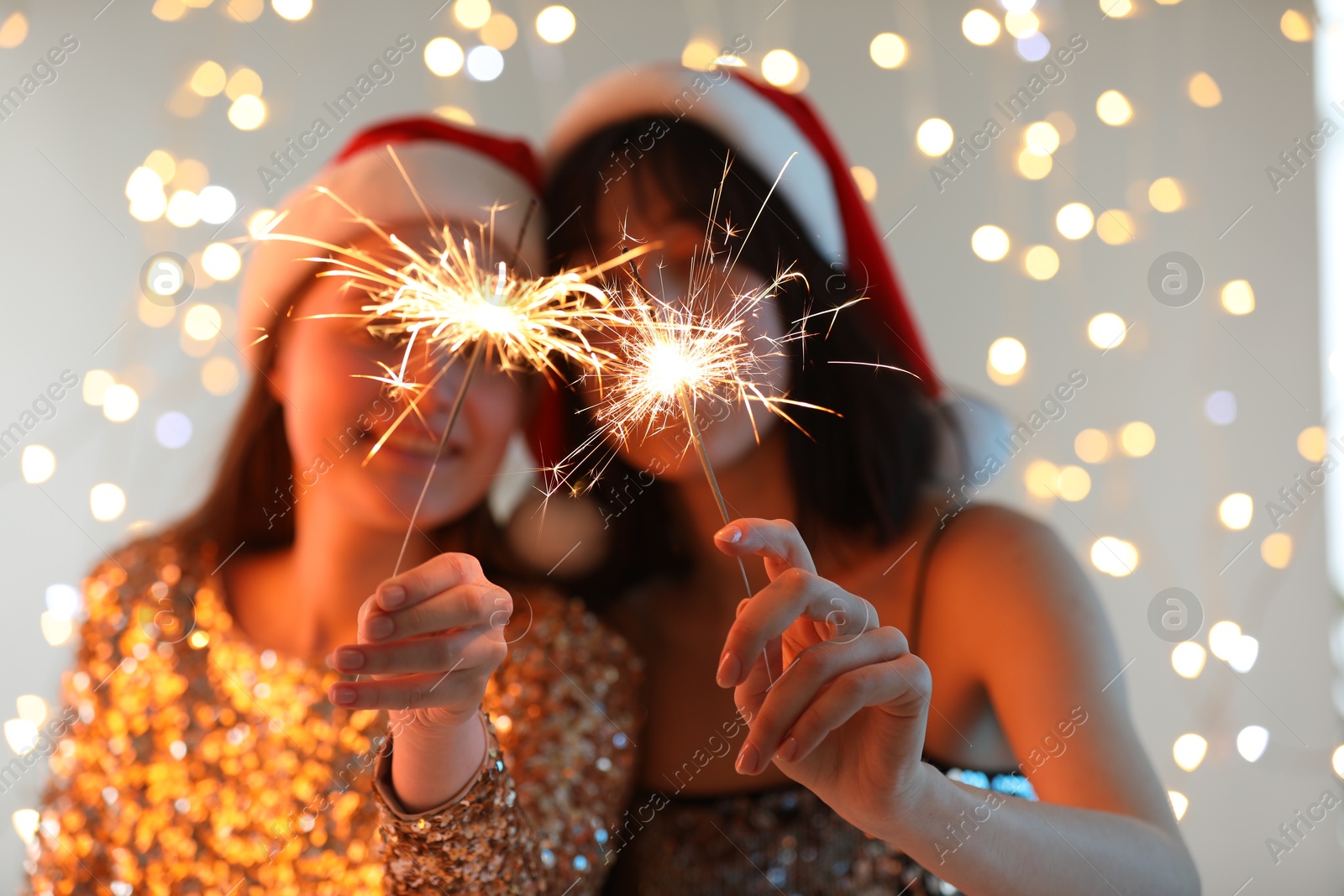 Photo of Women holding bright burning sparklers on background with blurred lights, selective focus