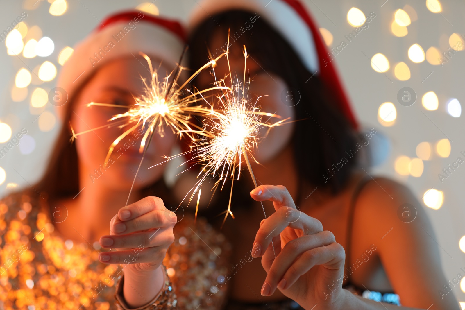 Photo of Women holding bright burning sparklers on background with blurred lights, selective focus