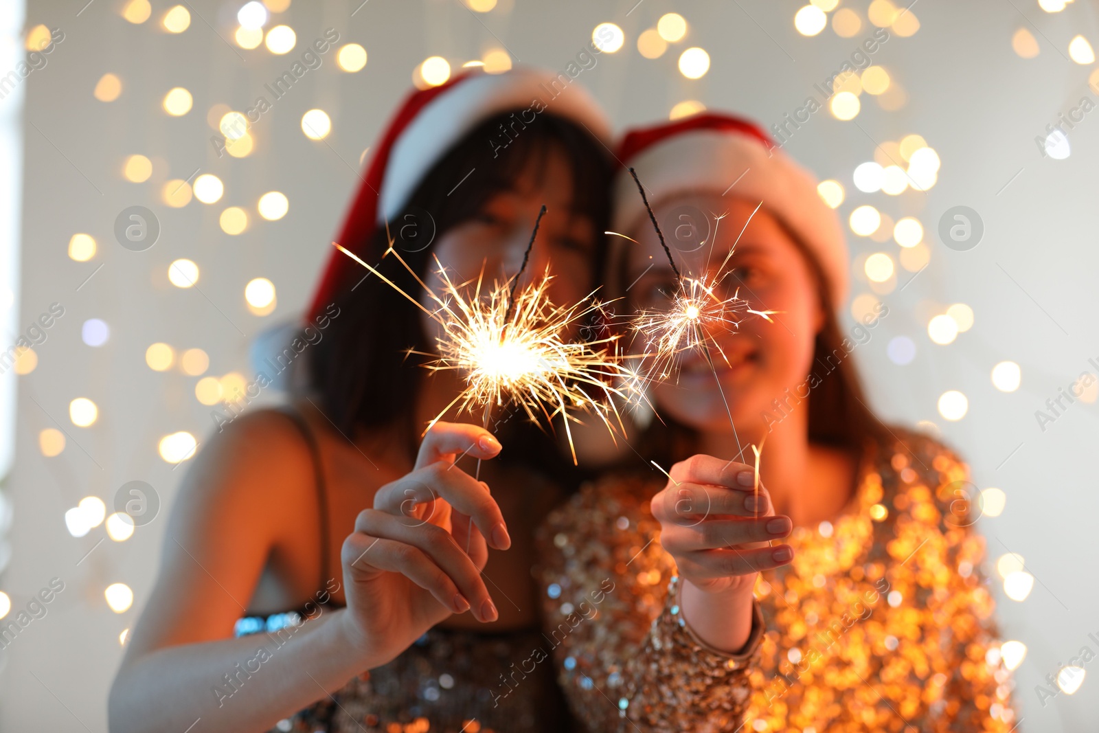 Photo of Women holding bright burning sparklers on background with blurred lights, selective focus