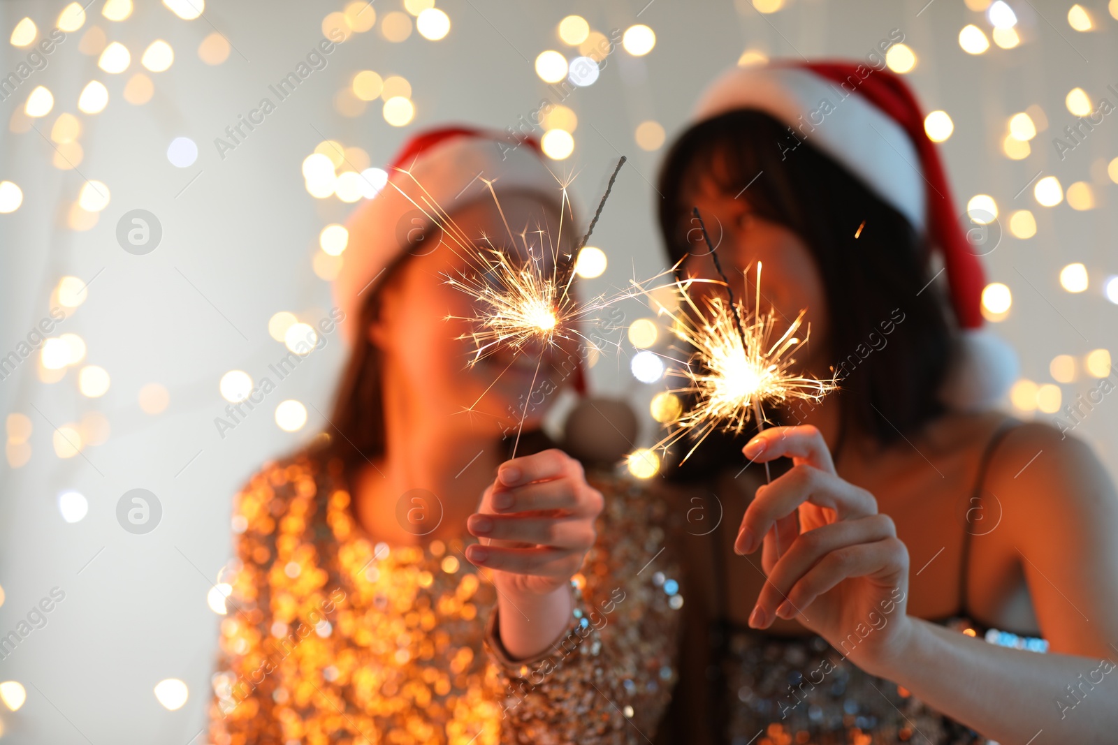 Photo of Women holding bright burning sparklers on background with blurred lights, selective focus