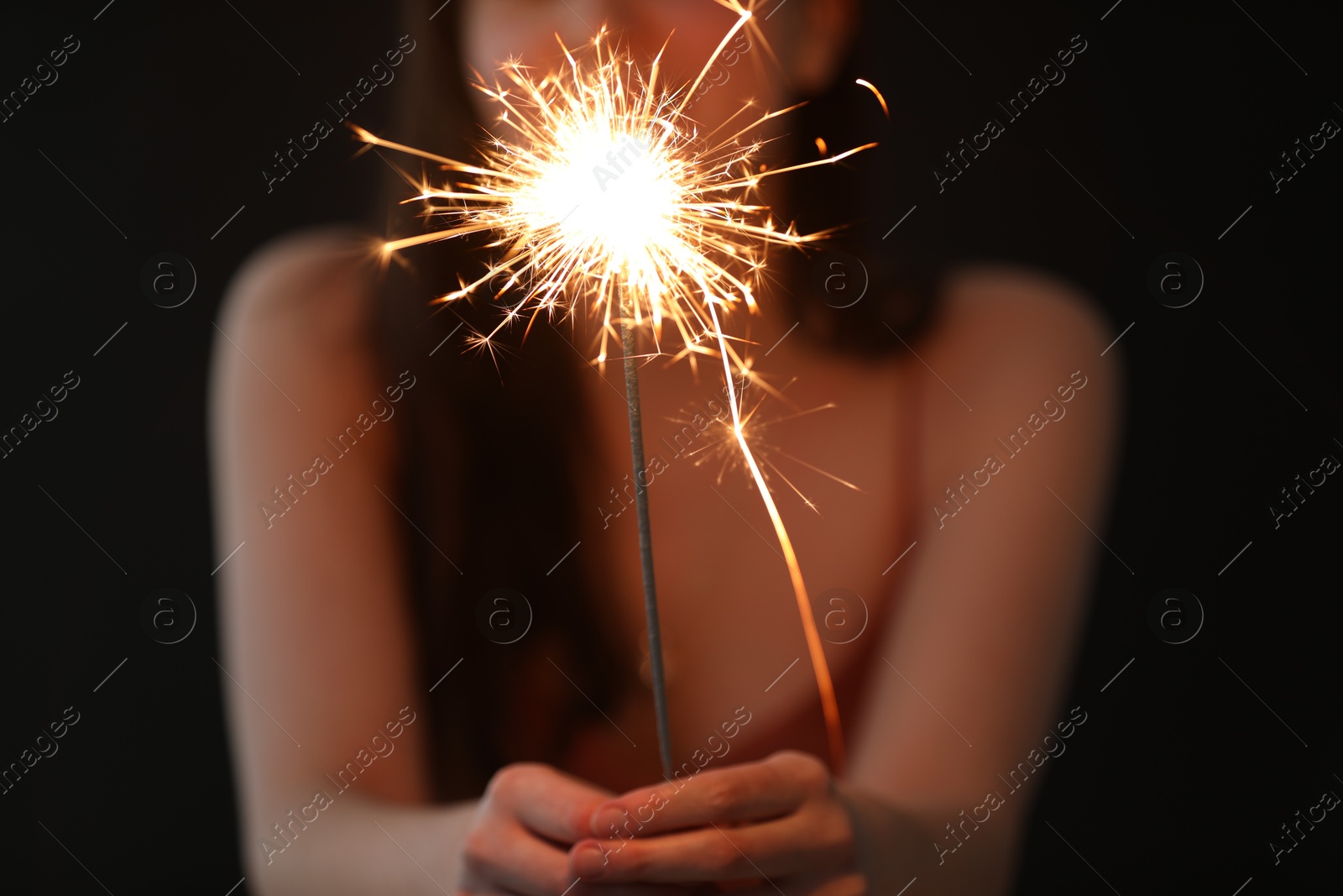 Photo of Woman with bright burning sparkler on black background, selective focus