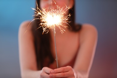 Photo of Woman with bright burning sparkler on color background, selective focus