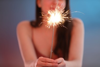 Photo of Woman with bright burning sparkler on color background, selective focus