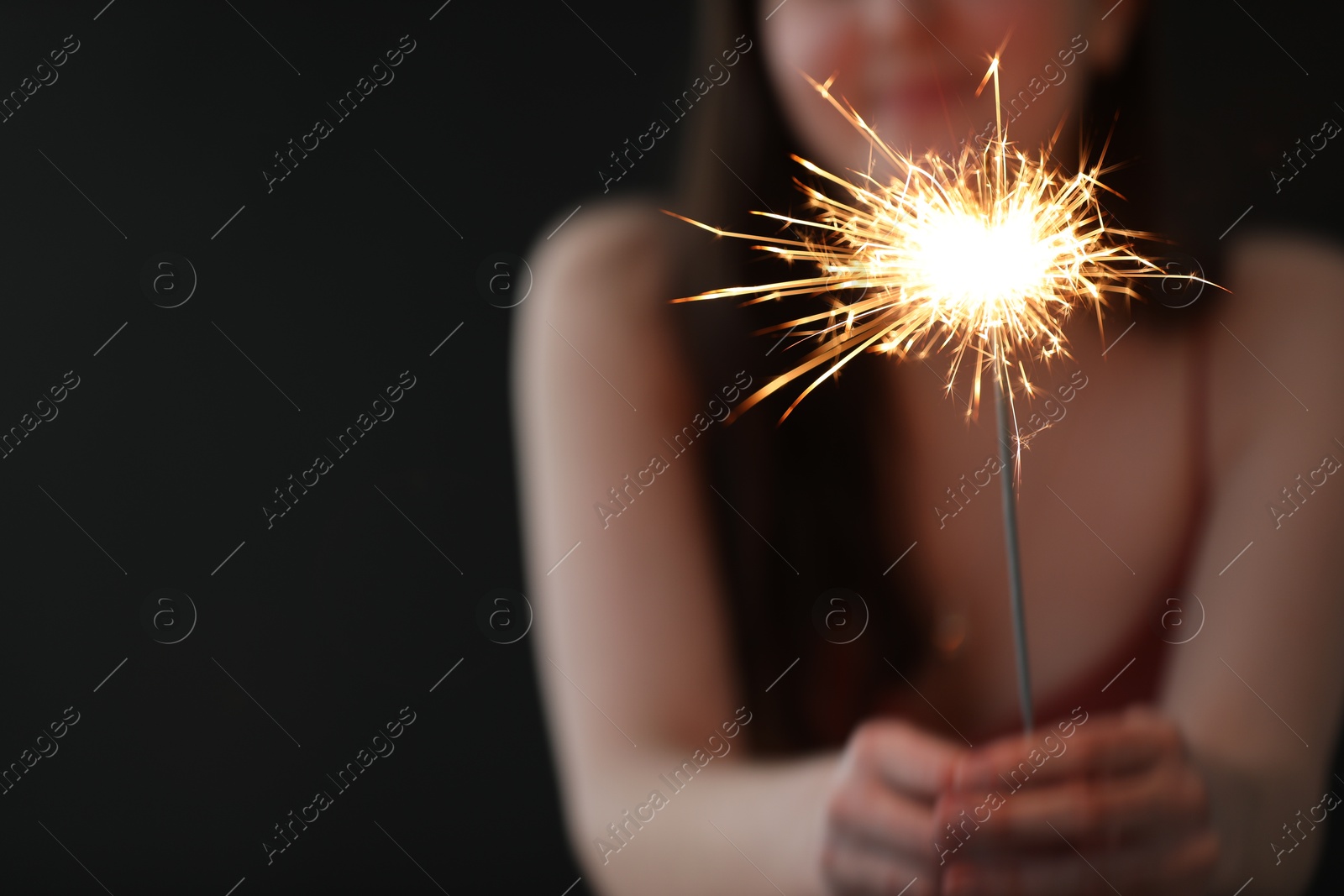 Photo of Woman with bright burning sparkler on black background, selective focus. Space for text