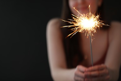 Photo of Woman with bright burning sparkler on black background, selective focus. Space for text