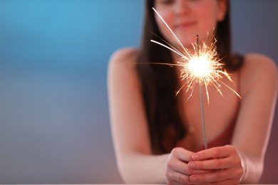 Photo of Woman with bright burning sparkler on color background, selective focus. Space for text