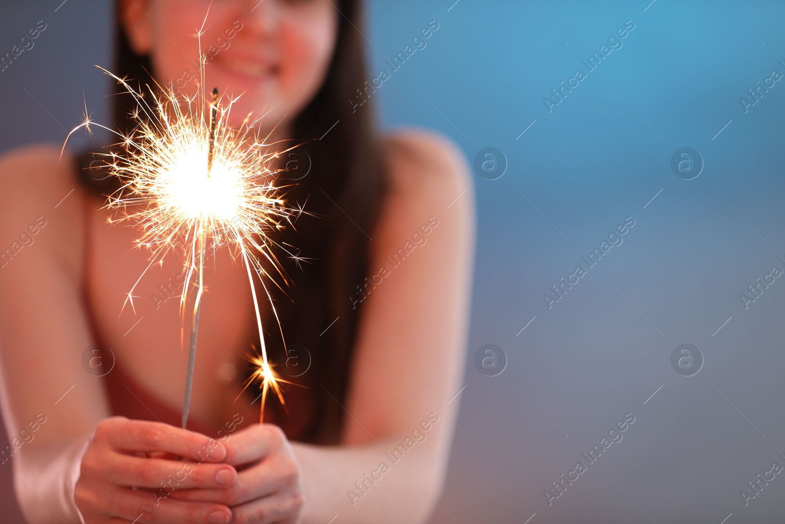 Photo of Woman with bright burning sparkler on color background, selective focus. Space for text