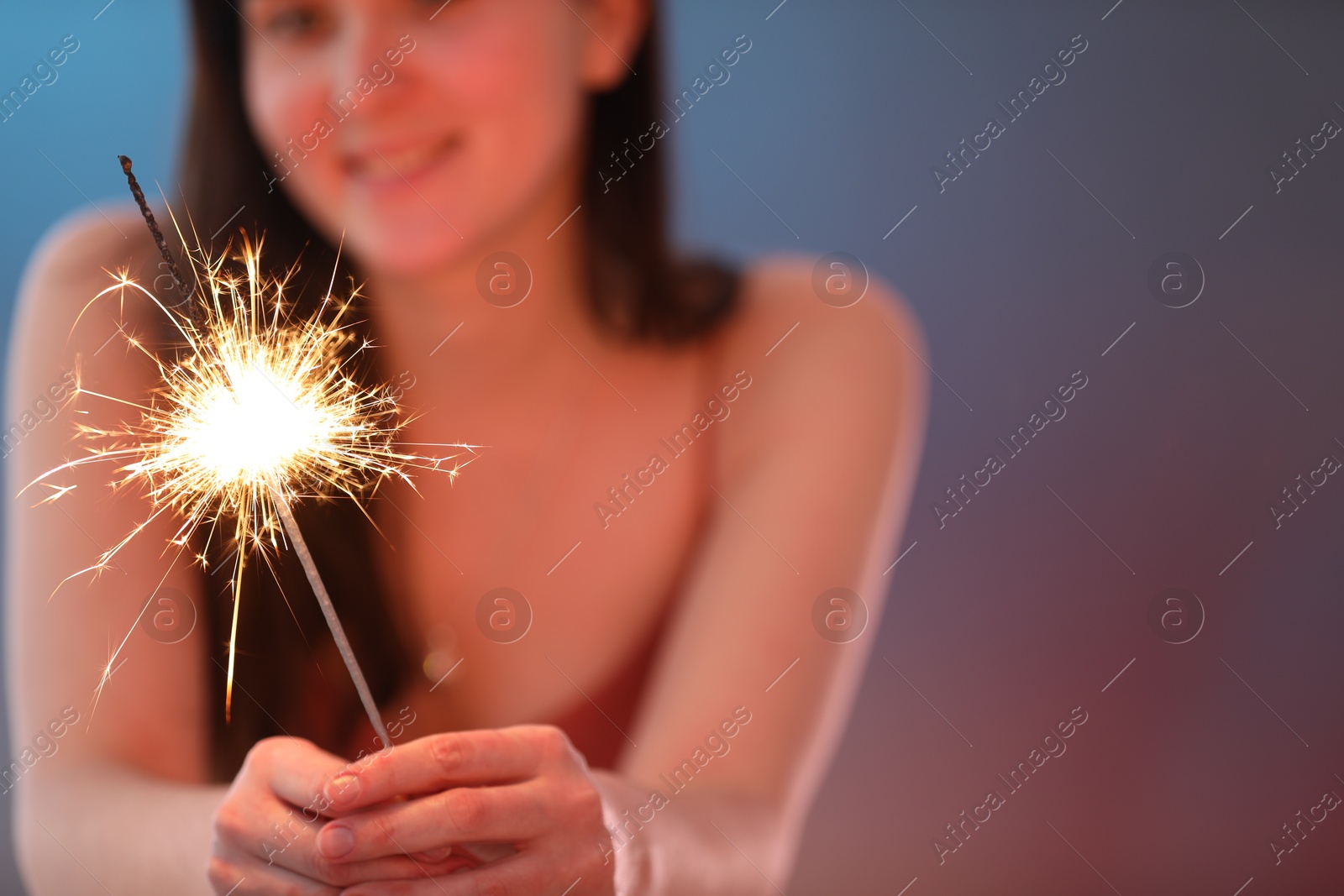 Photo of Woman with bright burning sparkler on color background, selective focus. Space for text