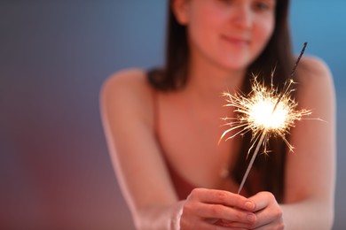 Photo of Woman with bright burning sparkler on color background, selective focus. Space for text