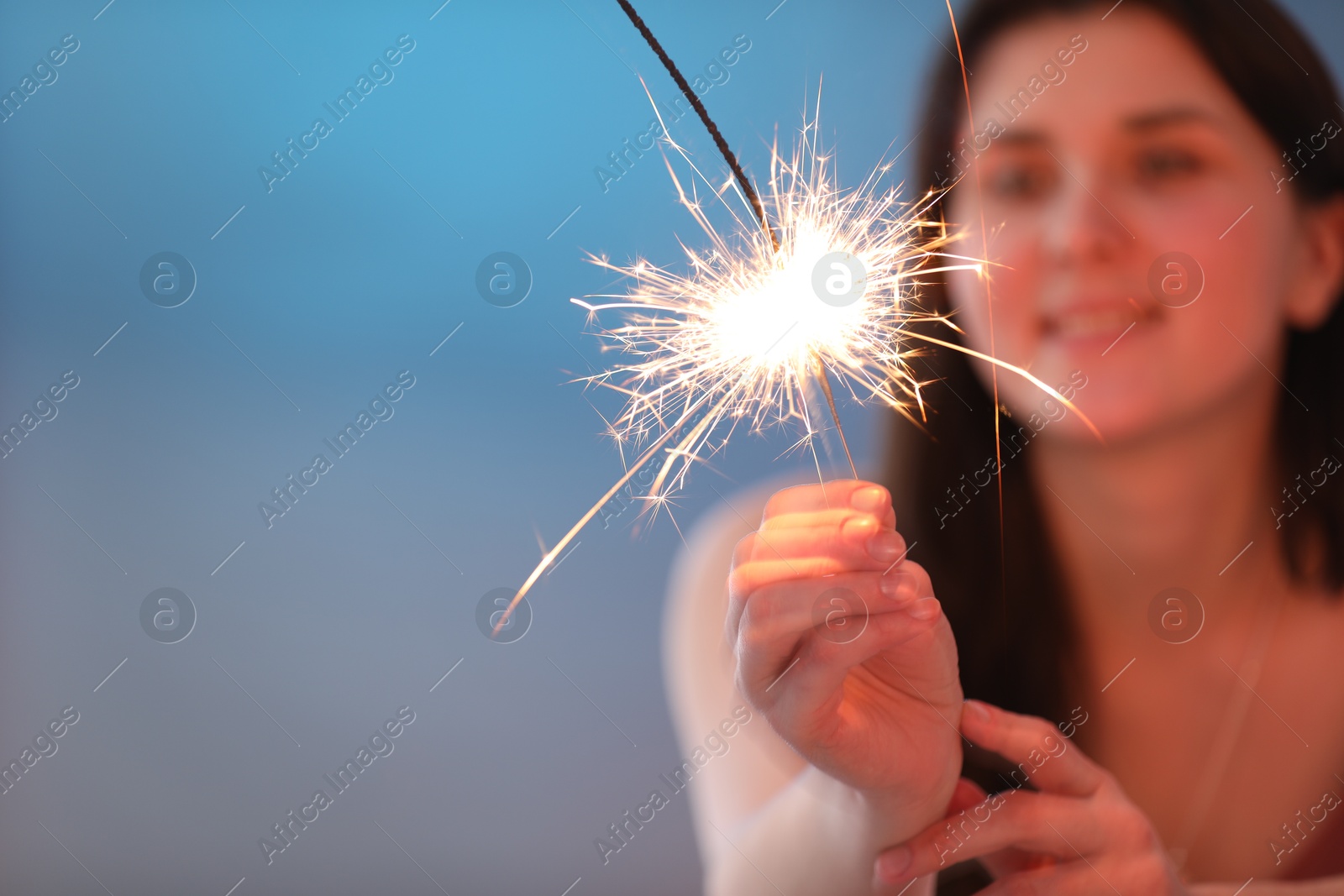 Photo of Woman with bright burning sparkler on color background, selective focus. Space for text