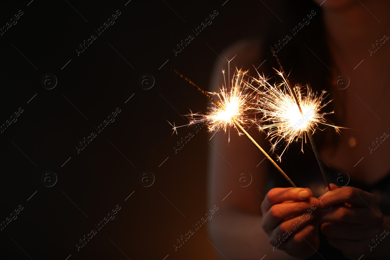 Photo of Woman with bright burning sparklers on dark background, closeup. Space for text