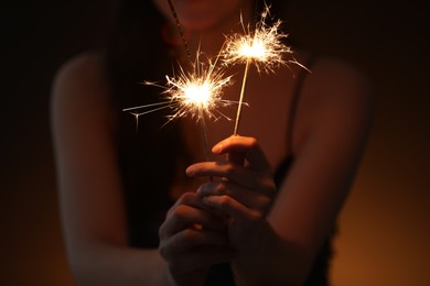 Photo of Woman with bright burning sparklers on dark background, closeup