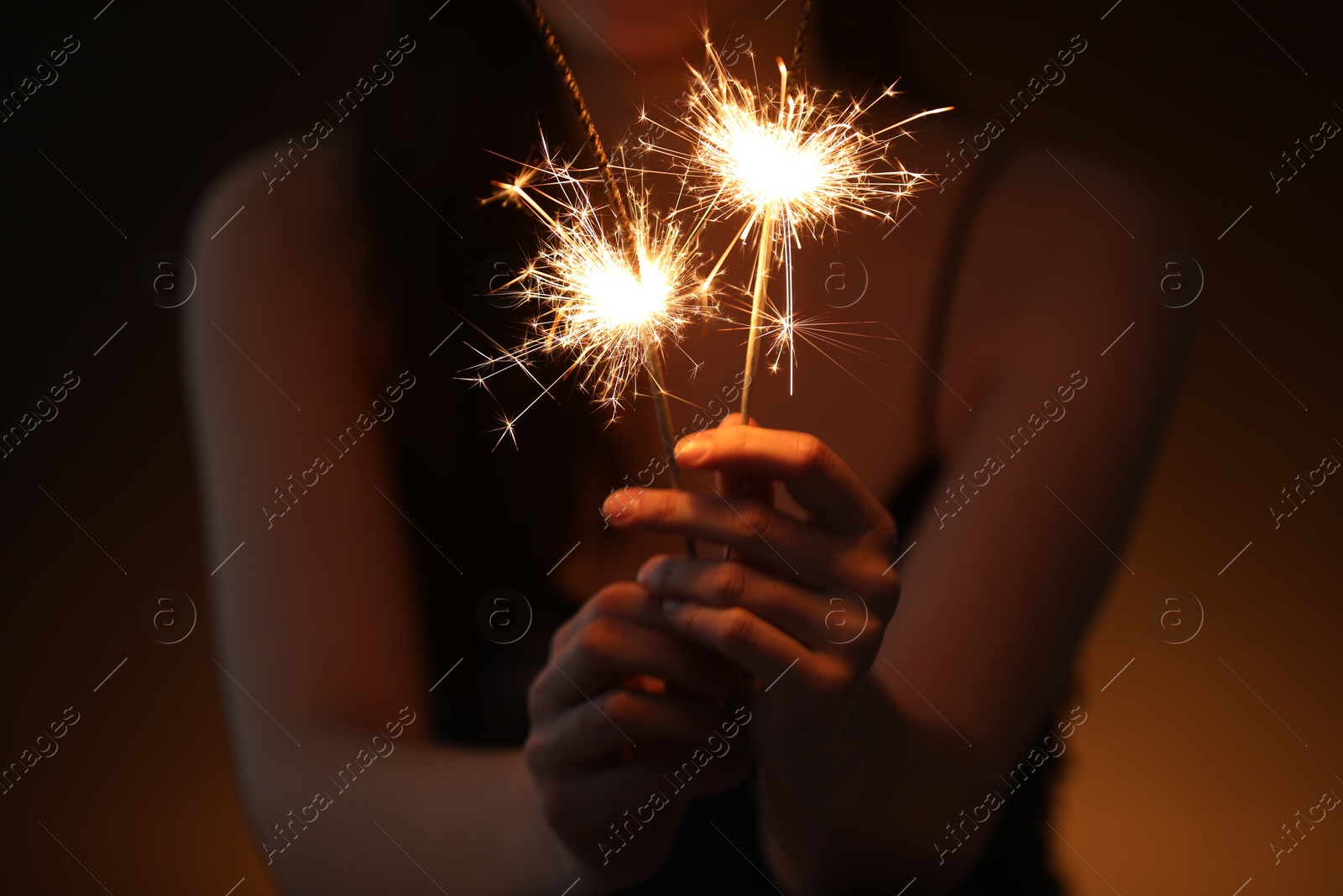 Photo of Woman with bright burning sparklers on dark background, closeup