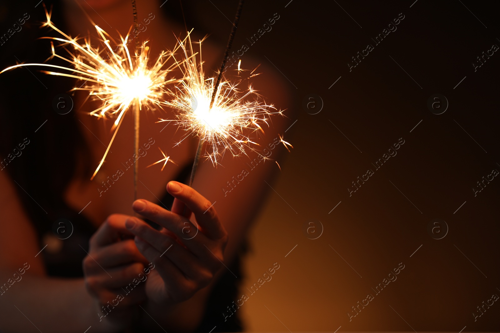 Photo of Woman with bright burning sparklers on dark background, closeup. Space for text