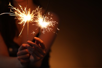 Photo of Woman with bright burning sparklers on dark background, closeup. Space for text