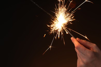 Photo of Woman with bright burning sparkler on dark background, closeup. Space for text