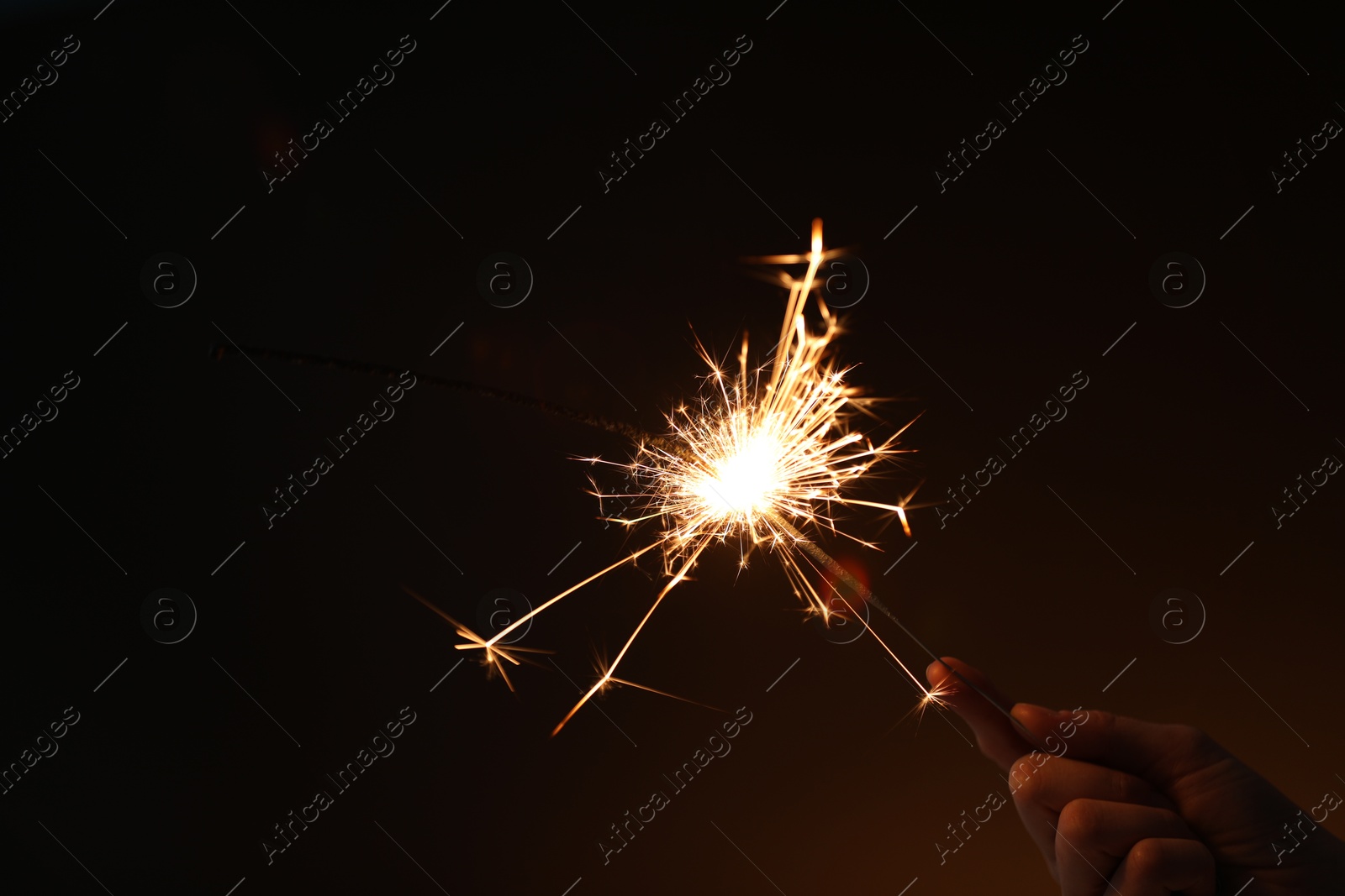 Photo of Woman with bright burning sparkler on dark background, closeup. Space for text