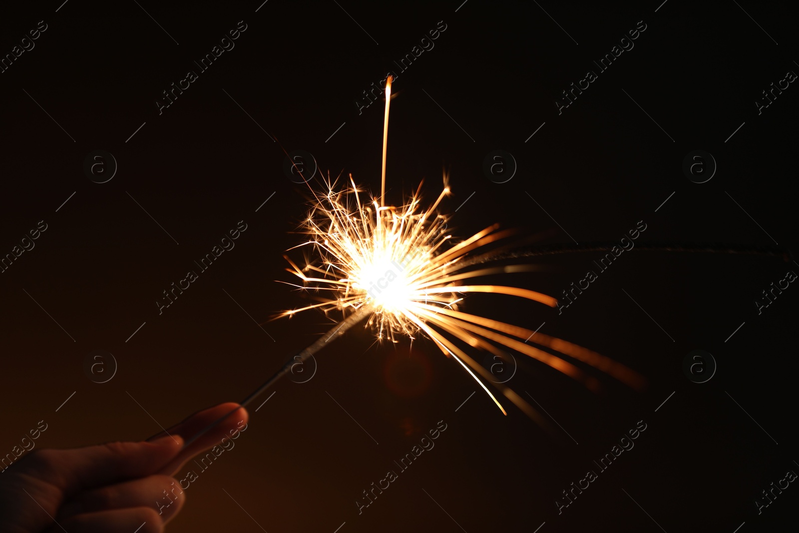 Photo of Woman with bright burning sparkler on dark background, closeup