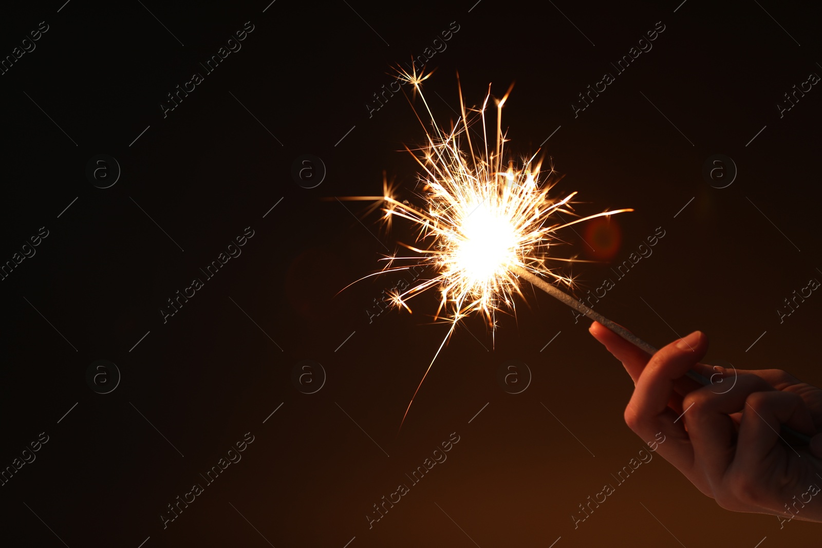 Photo of Woman with bright burning sparkler on dark background, closeup. Space for text