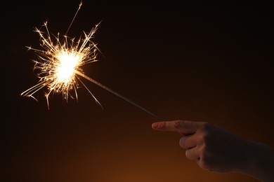 Photo of Woman with bright burning sparkler on dark background, closeup