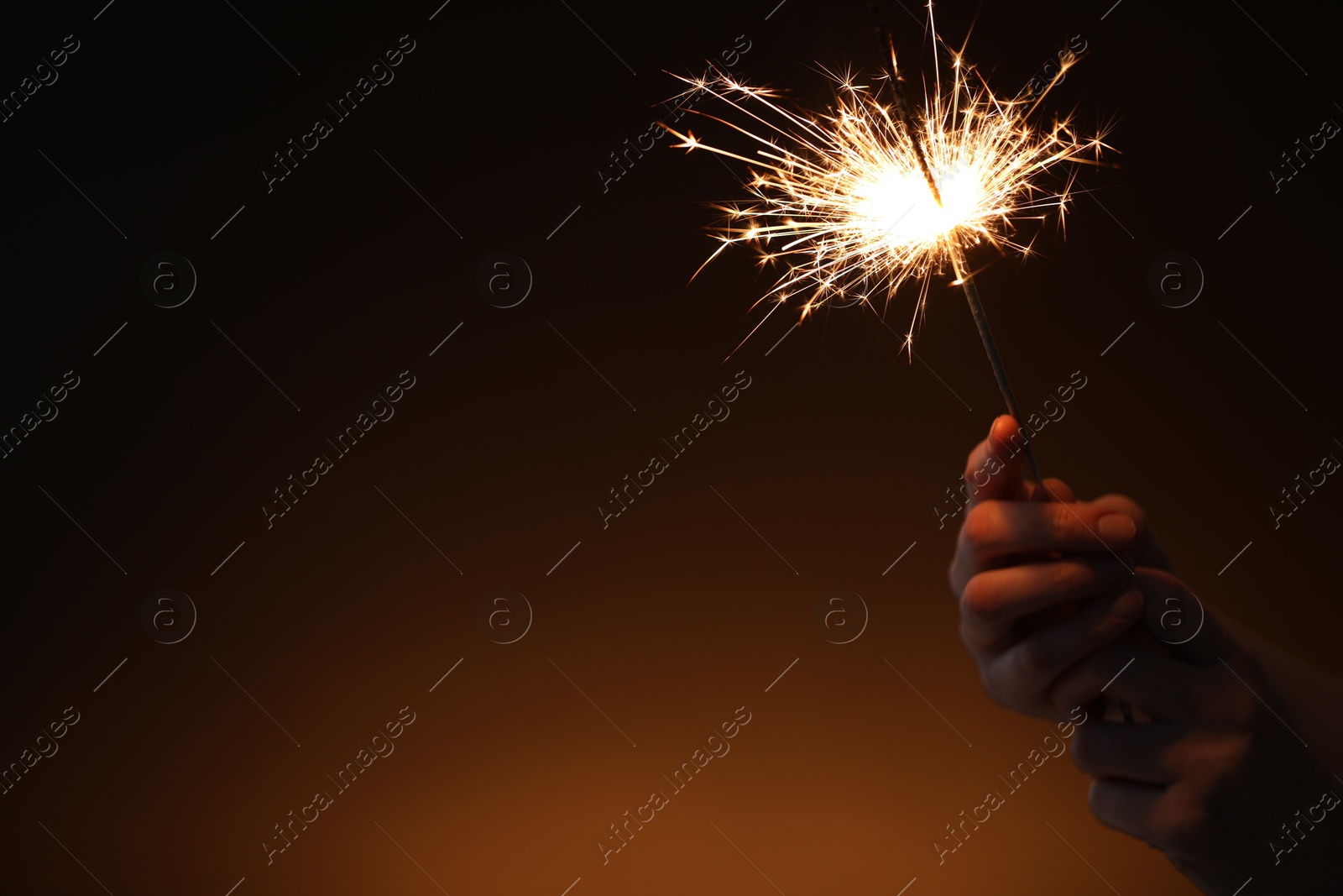 Photo of Woman with bright burning sparkler on dark background, closeup. Space for text