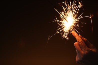 Photo of Woman with bright burning sparkler on dark background, closeup. Space for text