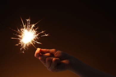 Photo of Woman with bright burning sparkler on dark background, closeup