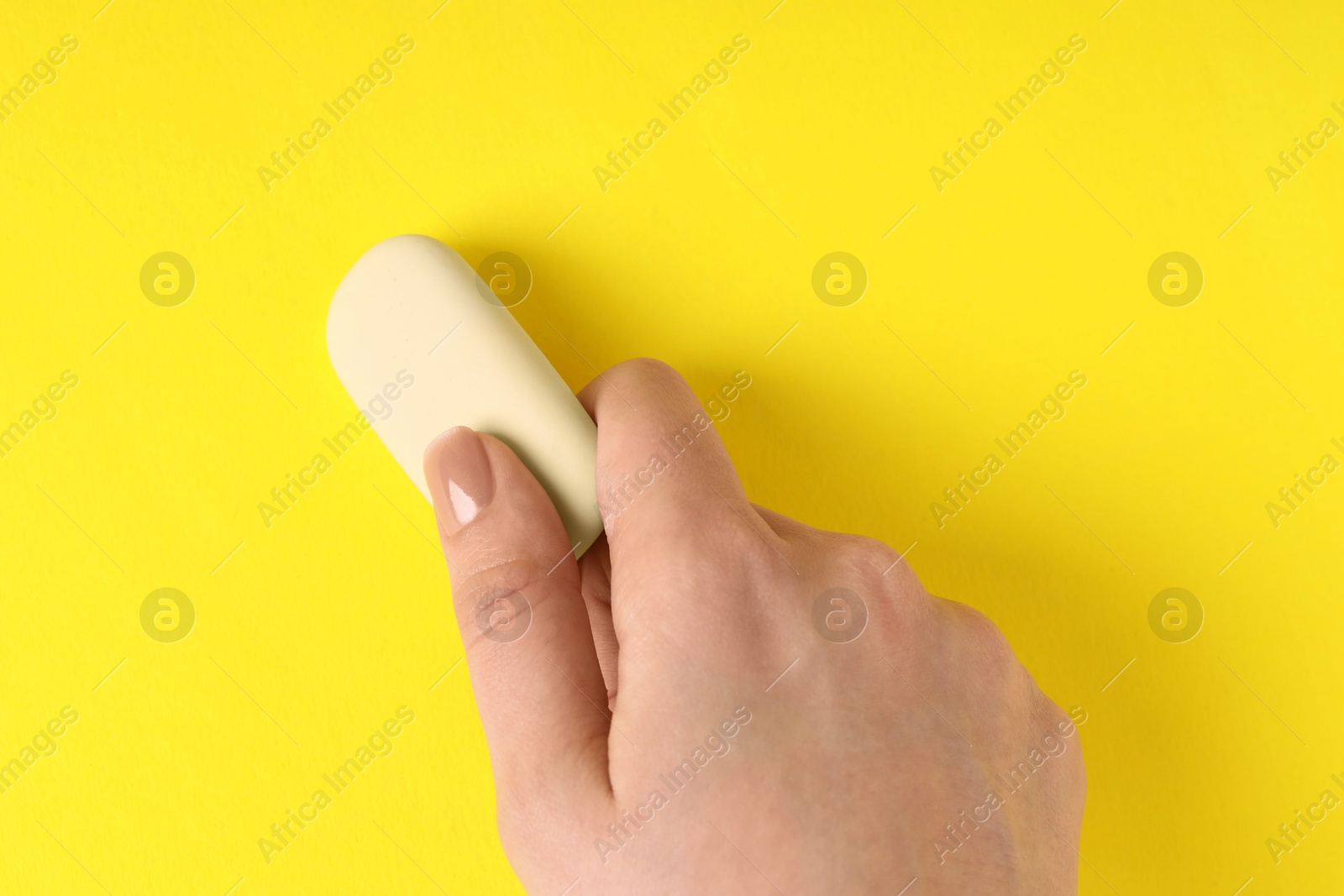 Photo of Woman using eraser on yellow background, closeup